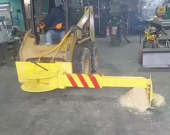 Minicargadora con brazo rastrillo extendido arrastrando una acumulación de material suelto en el piso del taller