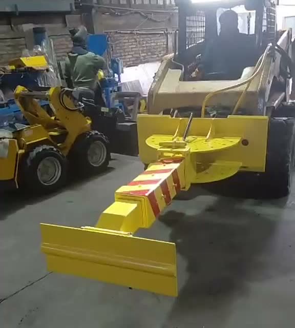Brazo rastrillo articulado amarillo, con franjas de seguridad rojas, montado en una minicargadora durante una prueba en taller